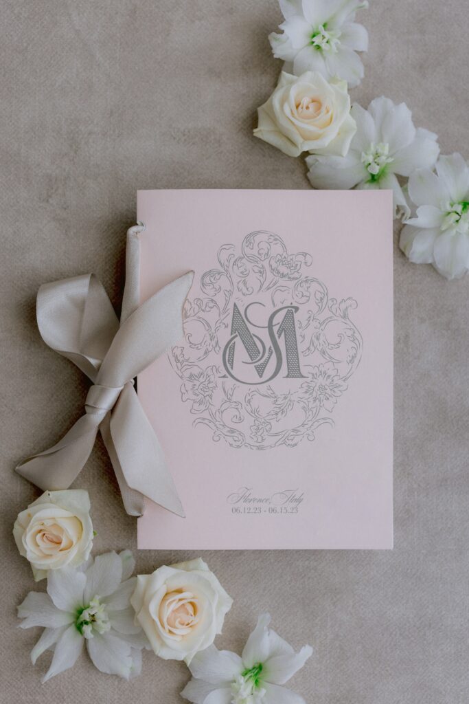 Pink wedding program booklet with ribbon on a brown background with flowers